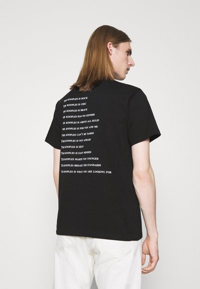 Schwarzes Baumwoll-T-Shirt mit weißem Text, der vertikal auf dem Rücken aufgedruckt ist, mit Phrasen wie "THE KOOPLES IS ROCK" und "THE KOOPLES HAS NO GENDER."