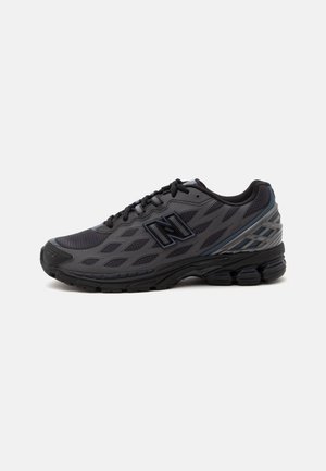 Ciemnoszary sportowy sneaker z czarną podeszwą, cholewką z siateczki i stylizowanym logo "N" po boku, pokazany z zewnętrznej strony na białym tle.