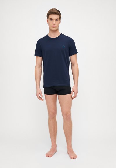 T-shirt blu navy a maniche corte realizzata in cotone, con scollo rotondo e un piccolo logo turchese sul petto, abbinata a pantaloni corta neri.