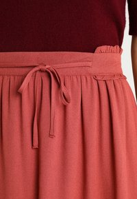 Gonna a vita alta, plissettata in un morbido tessuto corallo testurizzato. Caratterizzata da una cintura legata, una vita arrizzata e tasche laterali.