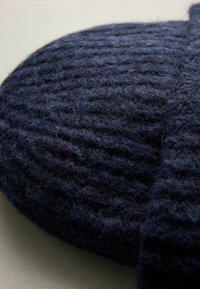 Granatowa, dzianinowa czapka beanie o prążkowanej fakturze, wykonana z miękkiej wełny, z podwiniętym brzegiem i delikatnymi odcieniami kolorów w całej powierzchni.