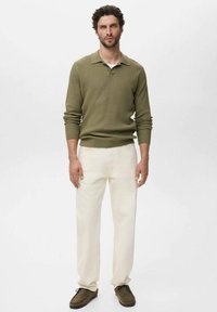 Polo shirt en tricot vert olive, pantalon crème, chaussures en suede marron. Design simple avec texture côtelée et col classique.