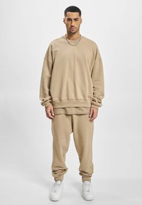 Beige oversized sweatshirt and tapered sweatpants in soft fabric. Features ribbed cuffs and a layered design. Paired with white sneakers.