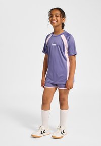 Lila sportigt tvådelat träningsset med rosa detaljer, kortärmad topp och shorts, kombinerat med vita knähöga strumpor och vita sneakers.