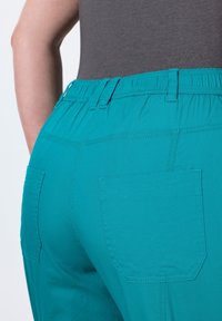 Pantaloni turchesi con fascia elastica in vita, dotati di due tasche posteriori e una texture liscia, che evidenziano un design aderente e cuciture pulite.