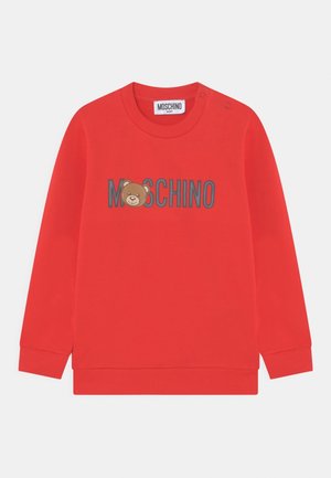 Czerwona bluza z prążkowanymi mankietami i dekoltem, z grafiką misia oraz napisem "MOSCHINO" w kolorze szarym nad grafiką. Dwa zatrzaski na ramieniu.