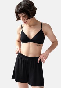 Zwarte bralette met verstelbare bandjes en een V-halsontwerp, gecombineerd met zwarte shorts met elastische tailleband, gemaakt van zachte, lichte stof.