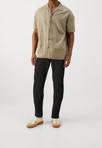 Krótka koszula na guziki w kolorze beżowym z kołnierzykiem z wycięciem, czarne spodnie o dopasowanym kroju oraz beżowe trampki z brązowymi akcentami i białymi detalami.