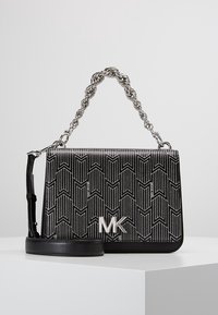 Borsa a mano con motivo bianco e nero, design geometrico, rifiniture in pelle e tracolla in metallo argentato. Presenta un logo argentato ben in vista.