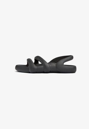 Black, flexible sandals featuring a wavy design with multiple cut-outs and a flat sole, made of smooth, rubber-like material.