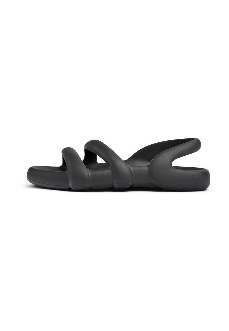 Black, flexible sandals featuring a wavy design with multiple cut-outs and a flat sole, made of smooth, rubber-like material.