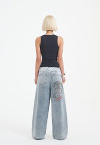 Jeans o szerokich nogawkach w jasnoniebieskim denimen z wyszywanym detalem smoka na tylnej kieszeni; zestawione z dopasowanym czarnym topem bez rękawów.