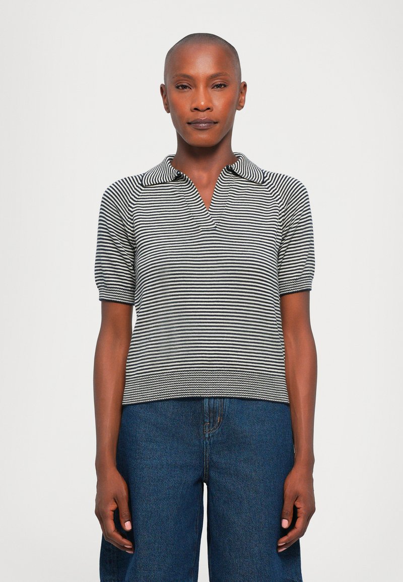 Black and white striped short-sleeve polo shirt with a collar. Fitted design and textured fabric. Worn with high-waisted blue denim pants.