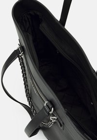 Sac à dos en cuir noir avec une surface texturée, poche zippée intérieure et une bandoulière accentuée de chaîne, présentant un intérieur spacieux et non doublé.