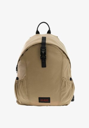 Sac à dos en nylon beige de forme arrondie, avec des accessoires noirs, une fermeture à boucle frontale et des poches latérales. Comprend une étiquette de marque au bas.