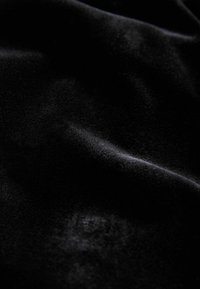 Schwarzer Samtstoff mit glatter Textur, der einen subtilen Glanz und sanft fließende Falten aufweist. Keine sichtbaren Muster oder Hardware-Details.