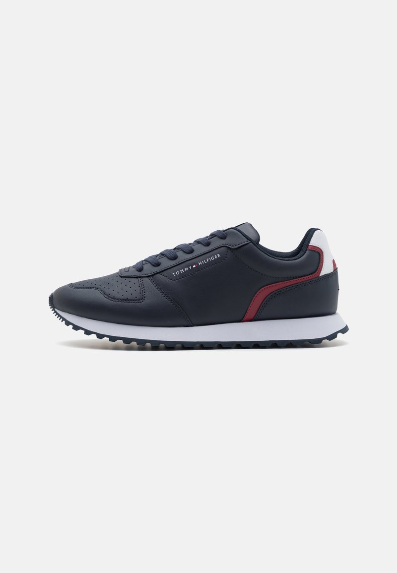 Marineblå sneakers lavet af syntetisk læder med en tekstureret overflade, der har røde og hvide detaljer, en hvid sål og runde snørebånd.