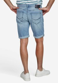 Jeans-Shorts mit einem hellblauen Waschung, umgeschlagenen Säumen und zwei Gesäßtaschen mit Steppnähten. Dazu weiße Sneaker.