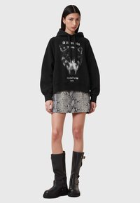 Sudadera negra con gráfico de lobo, combinada con una falda mini de estampado de serpiente y botas negras de caña alta con hebillas y suela texturizada.