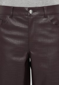 Burgundy műbőr nadrág krokodil mintával, elülső gombos záródással és zsebekkel. Simaság és fényes felület jellemzi.