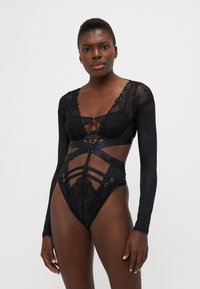 Zwart lingerieset met doorzichtige stof, kanten accenten, lange mouwen en geometrische banddetails met metalen hardware.