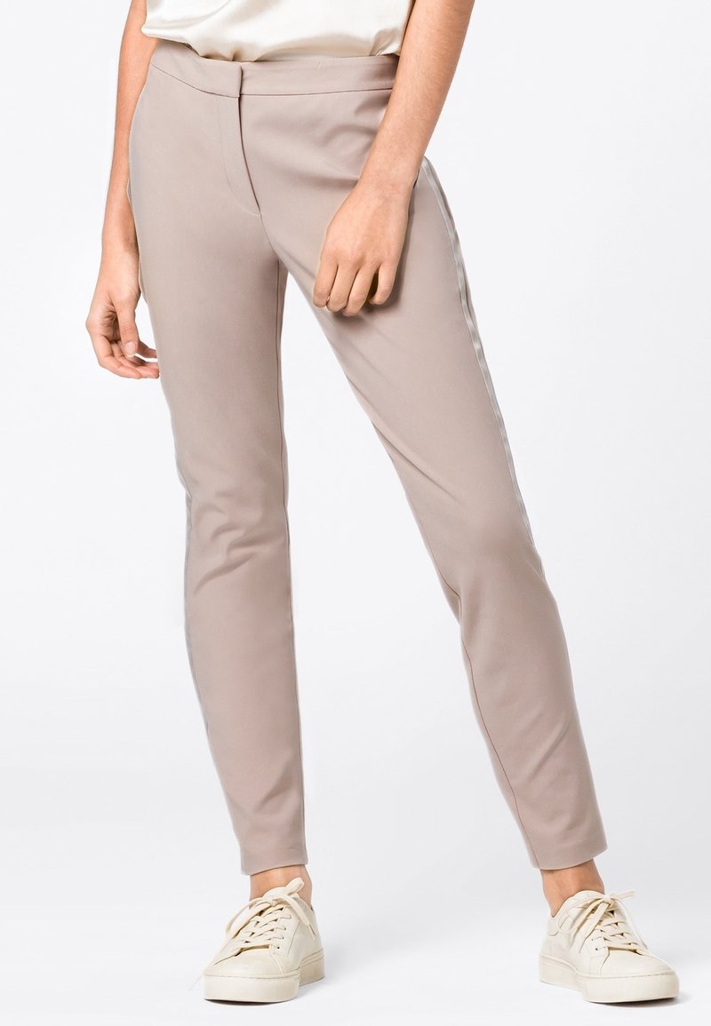 Pantalons slim beige clair en tissu doux, avec une texture lisse et des bandes latérales contrastantes, associés à des baskets blanches.