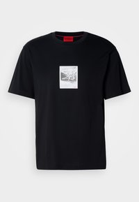 T-shirt nera in cotone con maniche corte, caratterizzata da una stampa grafica all'interno di una cornice rettangolare bianca. Accento del logo rosso in basso a destra.