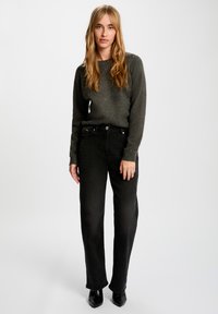 Suéter gris oscuro con acentos brillantes, combinado con jeans negros de pierna recta. El atuendo cuenta con un cuello redondo y un ajuste relajado. Zapatos negros de punta.