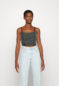 Top cropped preto e cinza com um padrão texturizado, apresentando alças finas. Combinado com jeans de cintura alta em azul claro.