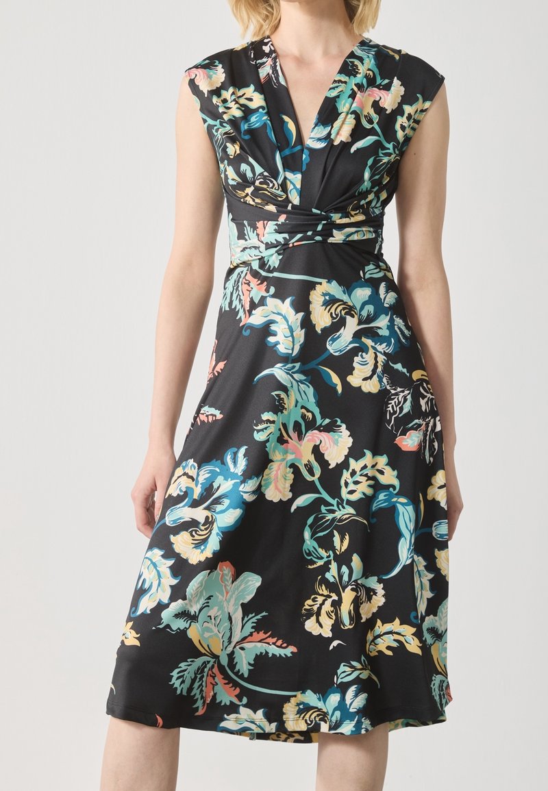 Robe noire sans manches avec un décolleté en V profond et un grand imprimé floral multicolore sur une jupe mi-longue fluide.