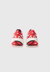 Scarpe da atletica rosse e bianche con una tomaia in rete, design sportivo, suola imbottita e motivi testurizzati distintivi sul tallone e sulla suola.