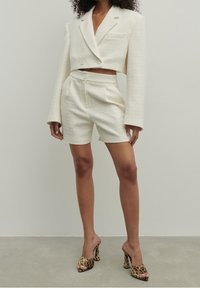 Kermatoisen värinen lyhyt blazer ja siihen sopivat mittatilaustyönä valmistetut shortit teksturoidusta kankaasta. Yhdistetty leopardikuosisilla korkokengillä.