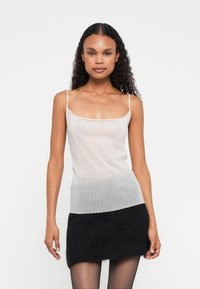 Lys grå strikket topp med tynne stropper, med ribbete tekstur nederst og glatt øverste del, kombinert med et svart luftig mini skjørt.