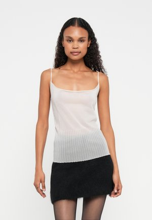 Gaiši pelēks adīts tops ar plānām siksnām, apakšā ar ribota tekstūra un gluda augšdaļa, kopā ar melnu pūkainu mini svārku.