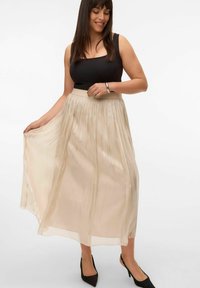Béžová maxi sukně s plisováním a přiléhavým pasem, vyrobená z lehkého materiálu. Černý top a špičaté lodičky doplňují outfit.