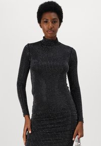 Long-sleeve black turtleneck dress adorned with silver studs, fitted shape, ribbed texture, and gathered detail at the waist.