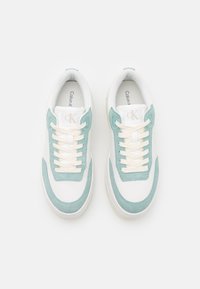 Sneakers bianchi con dettagli in suede verde menta, pelle texturizzata, lacci bianchi e un logo sulla linguetta. Vista dall'alto, design dalla forma arrotondata.
