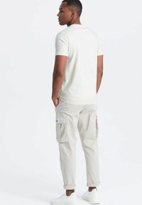 Camiseta de manga corta beige claro combinada con pantalones cargo beige claro que tienen bolsillos laterales. El modelo lleva zapatillas blancas. Textura de tela plana.