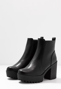 Mustat nahkasaappaat nilkkapituiset, joissa on paksu korko, pyöreä kärki, sileä pinta ja sivupullot. Värähtelevä pohja tarjoamaan pitoa.