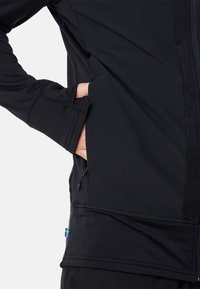 Zwarte softshell jas met een ritszak, textuurstof en contrasterende blauwe en gele Zweedse vlagdetail aan de zoom.