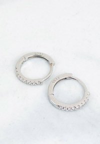 Silberne Creolen aus Sterlingsilber (S925) mit einer Reihe kleiner klarer Kristalle entlang einer Kante, kreisförmige Form, polierte Oberfläche.