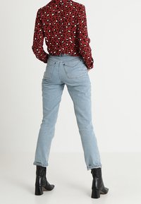 Chemisier à imprimé léopard rouge, jean taille haute bleu clair et bottes à talons noires. Le chemisier a des manches longues ; le jean est ajusté avec des poches arrière.