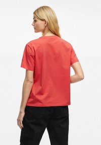 Koralfarvet bomulds t-shirt med korte ærmer, rund halsudskæring og en afslappet pasform. Bagsiden har et ensartet design uden mønstre eller detaljer.