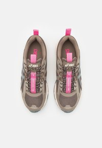 Brown athletic shoes with mesh upper, pink accents, and reflective details. Features a padded collar and tongue, with laces for secure fit.