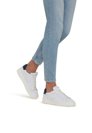 Weiße Leder-Sneaker mit navyblauem Fersenpatch, ausgestattet mit einer Schnürung und minimalistischen Design. Getragen mit hellen, eng geschnittenen Jeans.