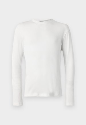 Chemise blanche à manches longues en côtes, avec encolure ras du cou, présentée sur un fond blanc.