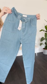 Pantalones de mezclilla azul claro con cintura alta, bolsillos delanteros y un acento en forma de anillo en la cintura. Textura suave con detalles de costura mínimos.