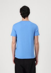 Hellblaues Baumwoll-T-Shirt mit kurzen Ärmeln, Rundhalsausschnitt und geradem Saum. Glatte Textur mit minimaler Ausstattung, getragen zu schwarzen Hosen.