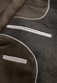 Tailored jacket interior with patterned brown lining, white piped pockets, and stitched detailing on wool fabric.