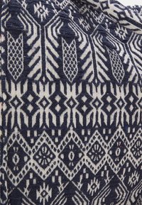 Textilie s modro-bílým geometrickým vzorem; zahrnuje šipky, diamanty a složité vzory s tkanou strukturou.